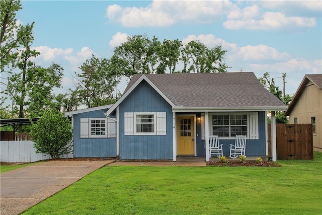 view of front of home with fence, roof with shingles, a porch, a front yard, and driveway