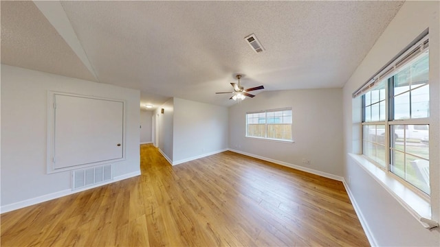 empty room with visible vents, a textured ceiling, lofted ceiling, and light wood-type flooring