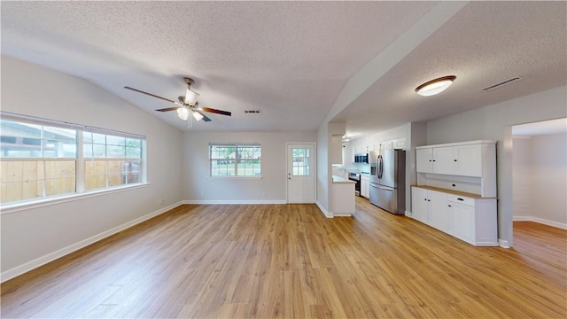 unfurnished living room with baseboards, a textured ceiling, a ceiling fan, light wood-style flooring, and vaulted ceiling
