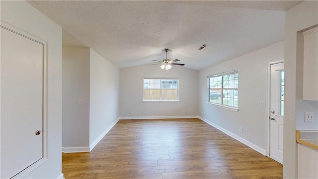 empty room featuring lofted ceiling, light wood-style floors, baseboards, a textured ceiling, and a ceiling fan