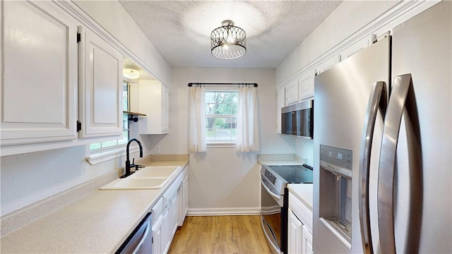 kitchen featuring stainless steel appliances, white cabinetry, a sink, and light wood-style floors