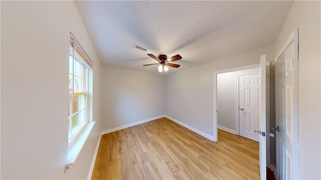 empty room featuring ceiling fan, light wood-type flooring, a textured ceiling, and visible vents
