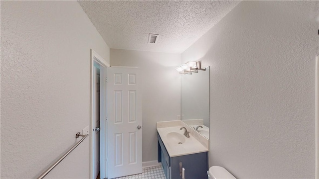 bathroom featuring visible vents, vanity, a textured wall, toilet, and a textured ceiling