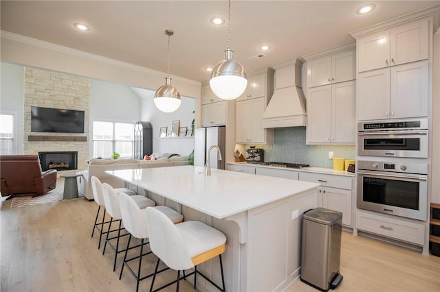 kitchen with crown molding, light countertops, premium range hood, a breakfast bar, and stainless steel appliances