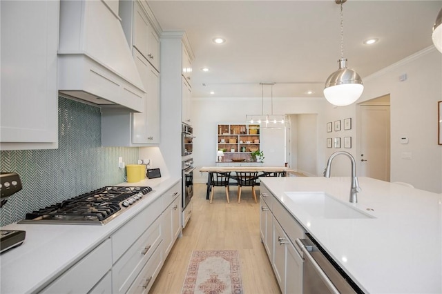 kitchen with premium range hood, light wood-type flooring, light countertops, a sink, and stainless steel appliances