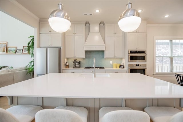 kitchen featuring crown molding, visible vents, an island with sink, custom range hood, and appliances with stainless steel finishes