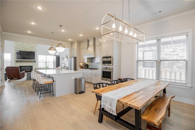 dining space with a stone fireplace, visible vents, ornamental molding, and light wood finished floors