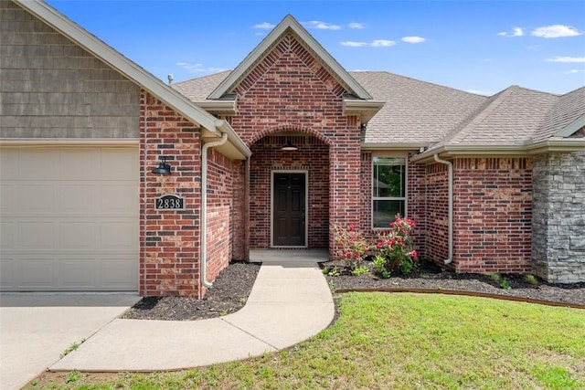 property entrance with an attached garage, roof with shingles, a yard, and brick siding