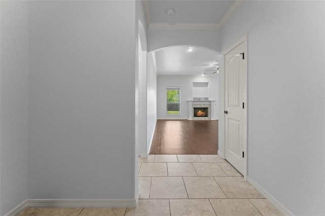 hallway with crown molding, arched walkways, light tile patterned floors, and baseboards