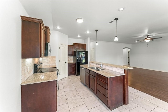 kitchen with a sink, an island with sink, ceiling fan, arched walkways, and appliances with stainless steel finishes