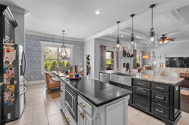 kitchen featuring ornamental molding, a center island with sink, wallpapered walls, a sink, and stainless steel appliances