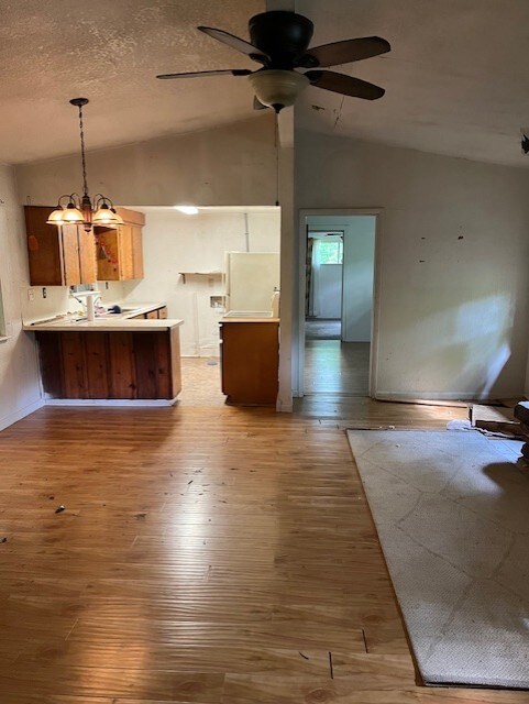 kitchen featuring hanging light fixtures, vaulted ceiling, ceiling fan with notable chandelier, a peninsula, and light wood-style floors