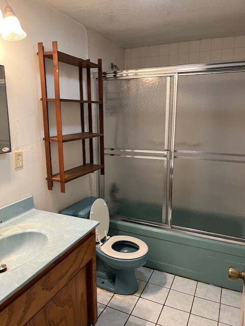 bathroom with tile patterned flooring, vanity, toilet, a textured ceiling, and bath / shower combo with glass door