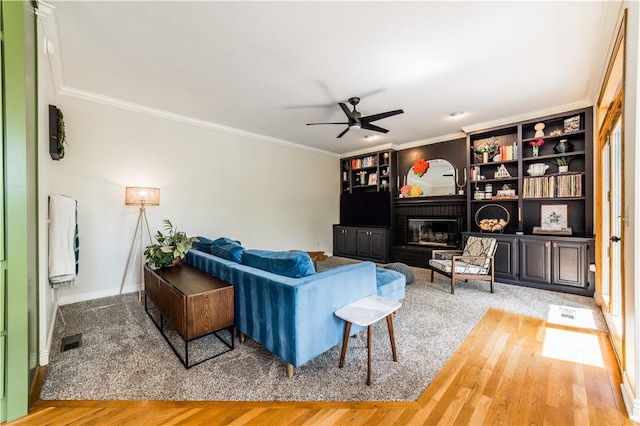 living room with ceiling fan, crown molding, wood finished floors, a brick fireplace, and baseboards