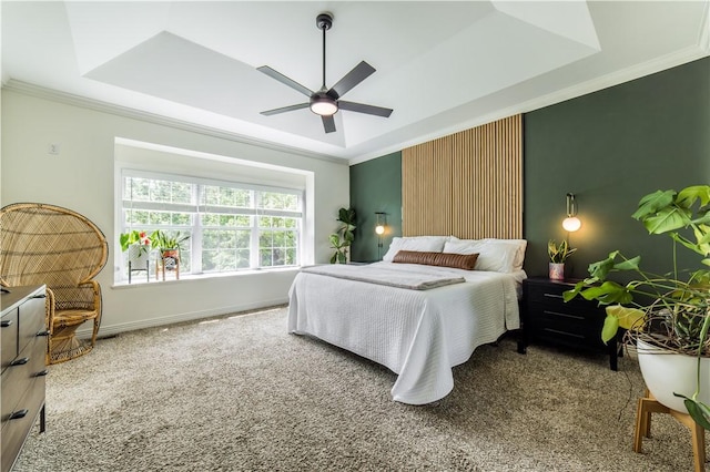 carpeted bedroom with a tray ceiling, ornamental molding, a ceiling fan, and baseboards