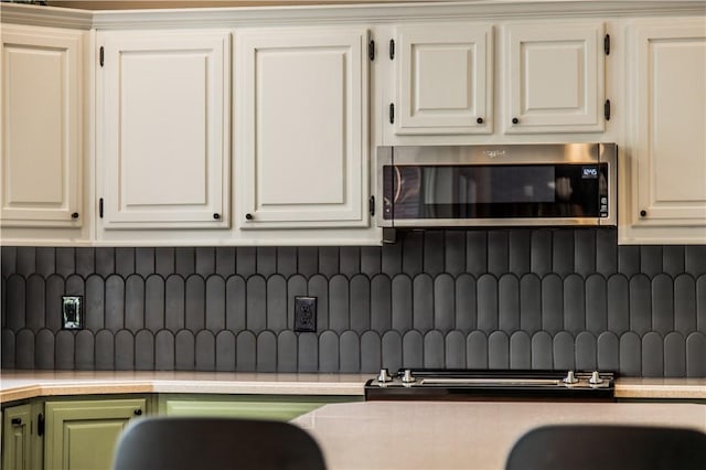 kitchen featuring stainless steel microwave, tasteful backsplash, light countertops, and white cabinets