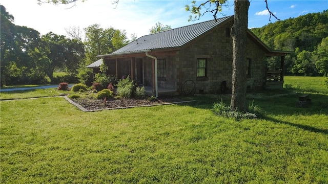 view of side of property featuring a lawn, a standing seam roof, metal roof, and stone siding