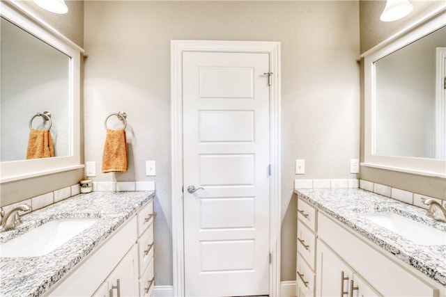 bathroom featuring baseboards, two vanities, and a sink