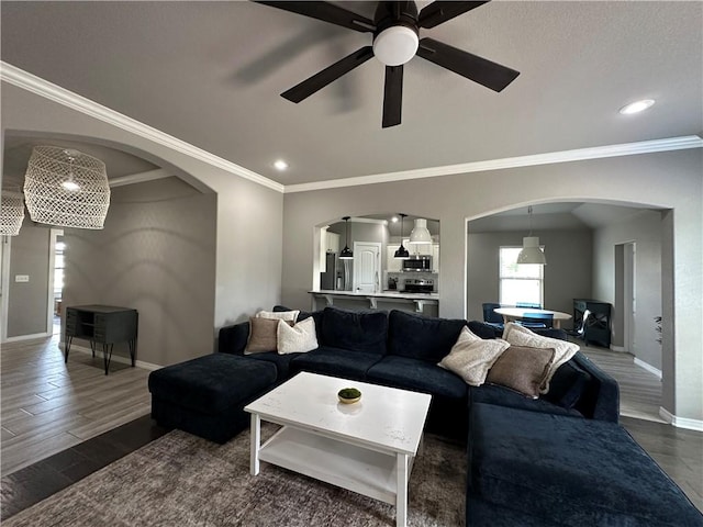 living room featuring arched walkways, baseboards, a ceiling fan, crown molding, and dark wood-style flooring