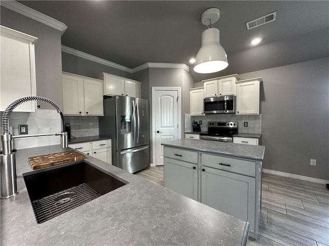 kitchen featuring stainless steel appliances, a sink, backsplash, ornamental molding, and white cabinetry