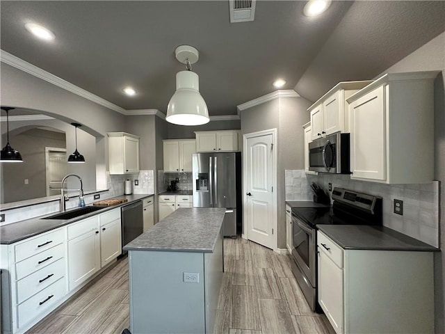 kitchen featuring appliances with stainless steel finishes, a sink, dark countertops, ornamental molding, and a center island