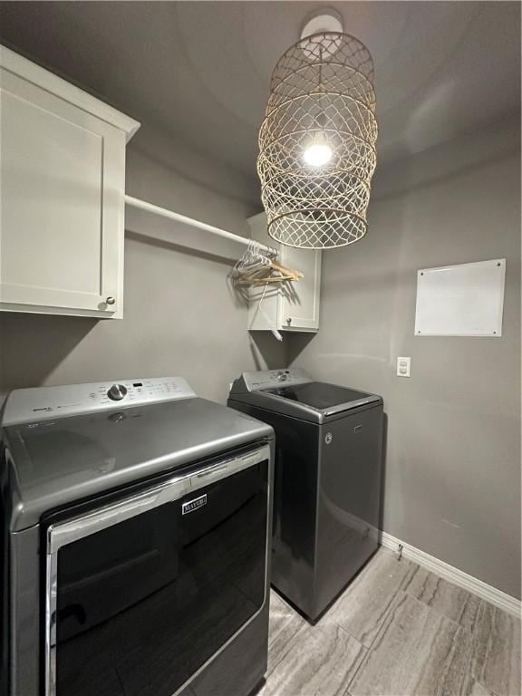 clothes washing area featuring washing machine and clothes dryer, light wood-style flooring, baseboards, and cabinet space