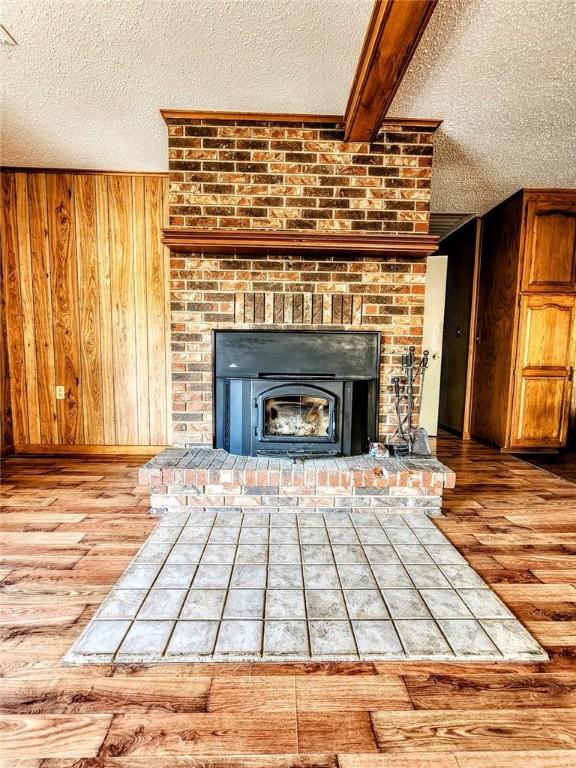 details with wooden walls, a textured ceiling, a brick fireplace, and wood finished floors