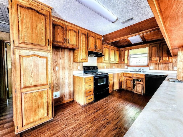 kitchen with wooden walls, light countertops, under cabinet range hood, visible vents, and black appliances