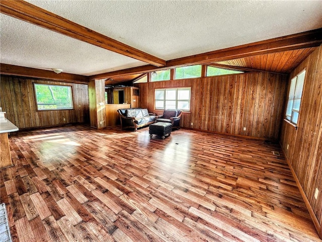 living area with a textured ceiling, beamed ceiling, wood walls, and wood finished floors