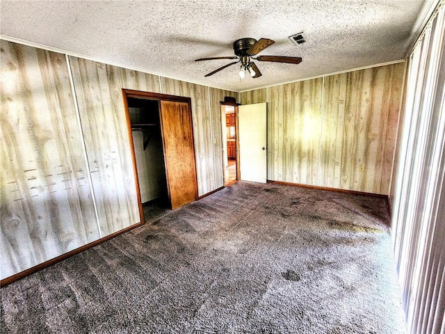 unfurnished bedroom featuring carpet flooring, wood walls, visible vents, and a closet
