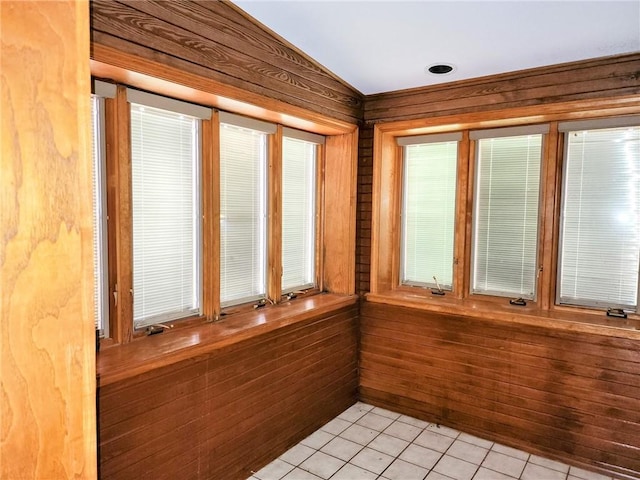 unfurnished sunroom featuring wooden walls, lofted ceiling, and tile patterned flooring