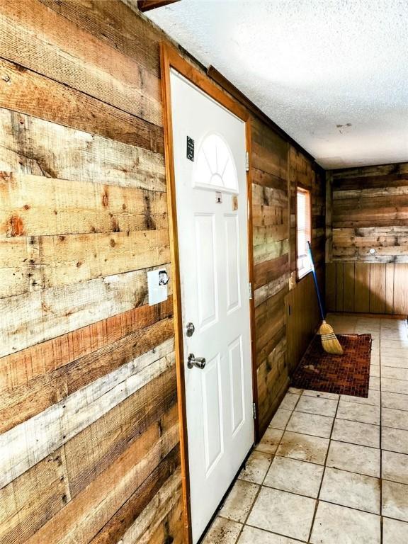 doorway featuring wooden walls, light tile patterned floors, a textured ceiling, and a healthy amount of sunlight