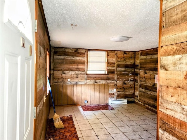 unfurnished room with wood walls, a textured ceiling, and light tile patterned floors