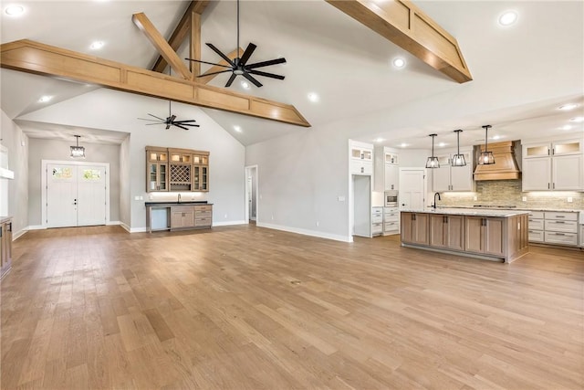 unfurnished living room with a ceiling fan, beam ceiling, baseboards, a sink, and light wood finished floors