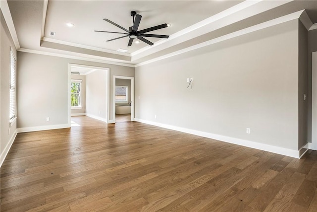 spare room with a ceiling fan, crown molding, wood finished floors, baseboards, and a tray ceiling
