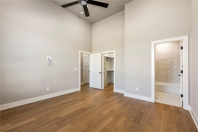 unfurnished bedroom with wood finished floors, baseboards, a walk in closet, high vaulted ceiling, and connected bathroom