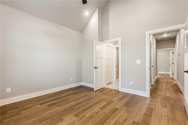 unfurnished bedroom with visible vents, light wood finished floors, baseboards, and high vaulted ceiling