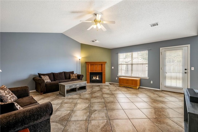 living area with visible vents, ceiling fan, a lit fireplace, a textured ceiling, and vaulted ceiling