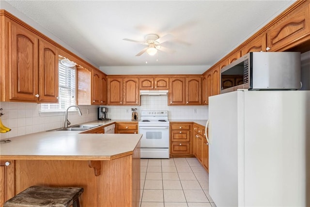 kitchen featuring brown cabinetry, a ceiling fan, a peninsula, white appliances, and a sink