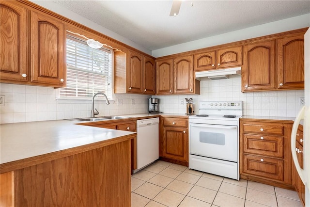 kitchen with a sink, brown cabinetry, under cabinet range hood, and white appliances