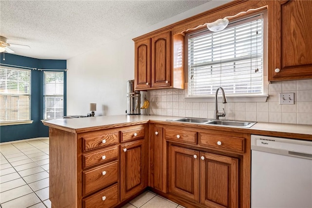 kitchen with brown cabinets, white dishwasher, a sink, light countertops, and a ceiling fan
