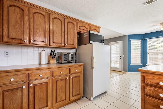 kitchen with visible vents, freestanding refrigerator, a toaster, brown cabinets, and light tile patterned floors