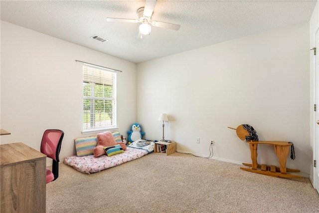 recreation room with carpet floors, a textured ceiling, a ceiling fan, baseboards, and visible vents