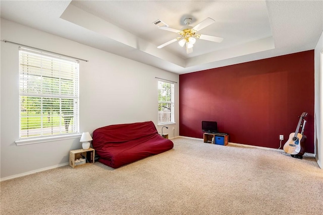 living area featuring baseboards, carpet flooring, a ceiling fan, and a tray ceiling