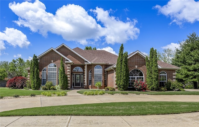 view of front of property featuring a front lawn, brick siding, roof with shingles, and a garage