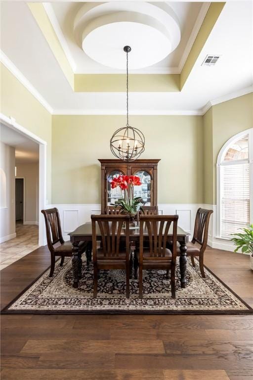 dining space with a notable chandelier, ornamental molding, wainscoting, visible vents, and a raised ceiling