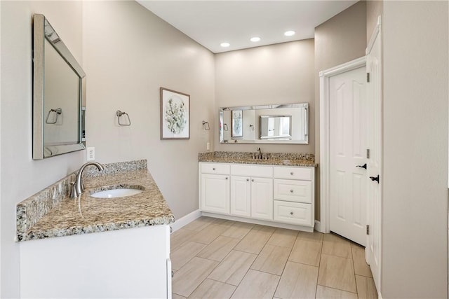 bathroom featuring baseboards, recessed lighting, two vanities, and a sink