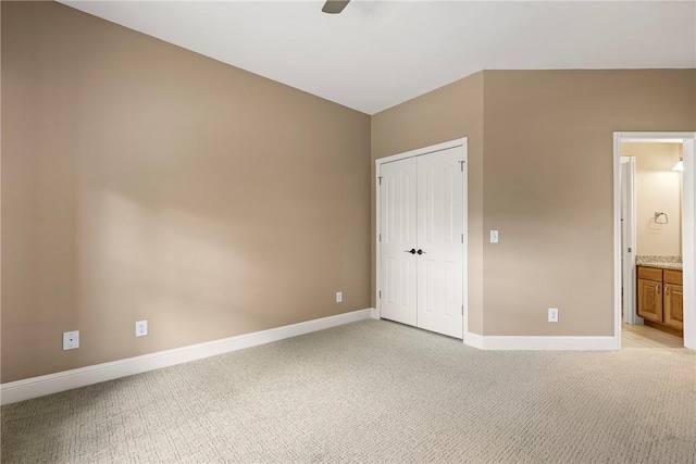 unfurnished bedroom with a closet, light colored carpet, ensuite bath, a ceiling fan, and baseboards