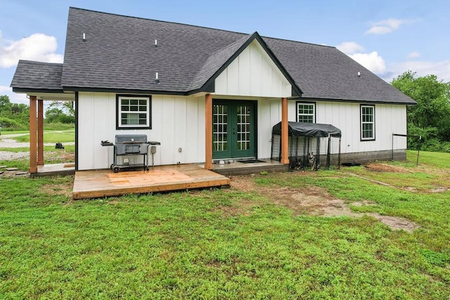 rear view of property featuring a wooden deck, french doors, a shingled roof, board and batten siding, and a yard