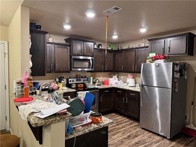 kitchen featuring dark brown cabinets, light stone counters, light wood finished floors, stainless steel appliances, and visible vents